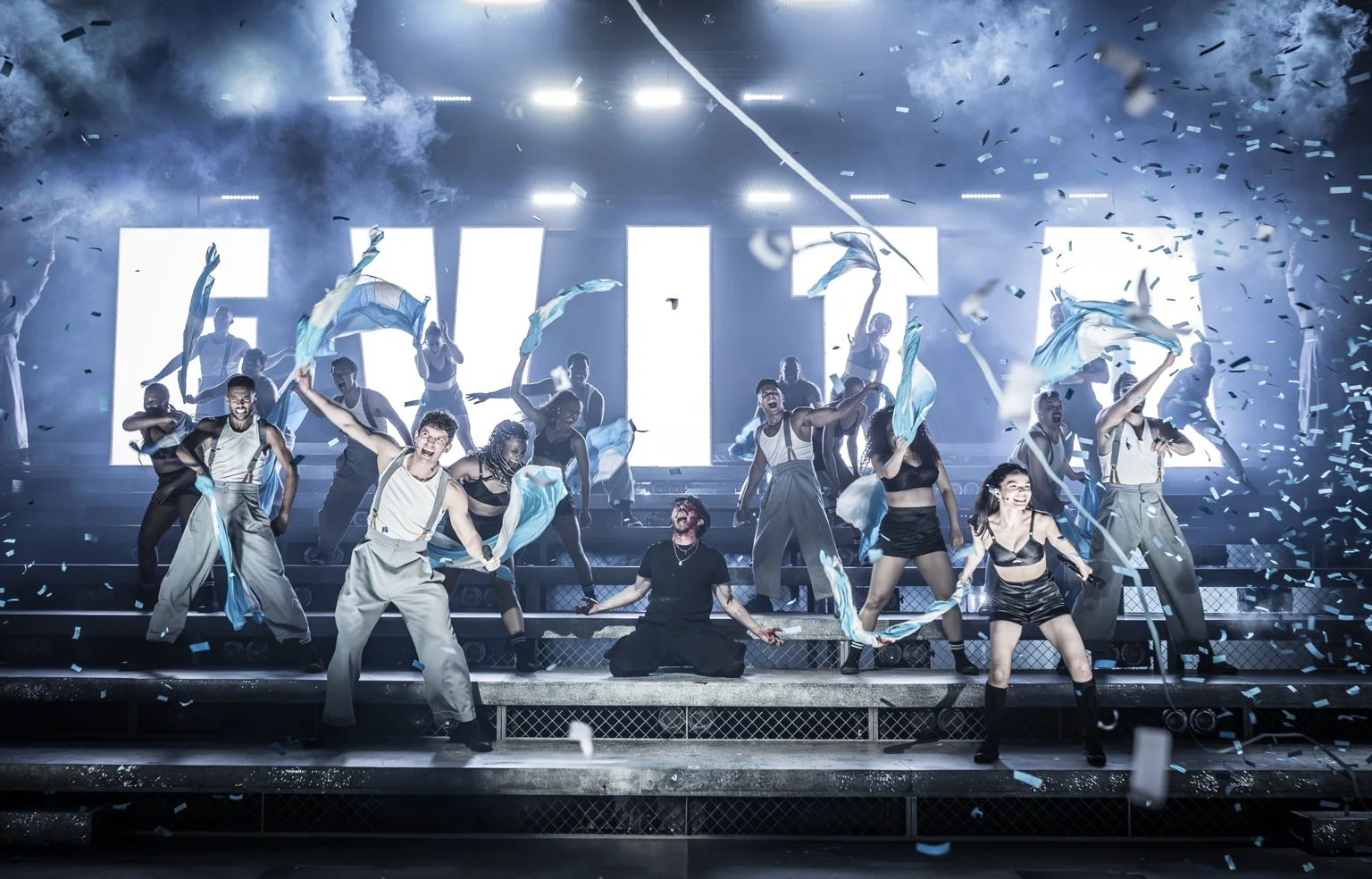 The company of Evita performs amid bright stage lights, smoke and confetti at the London Palladium.