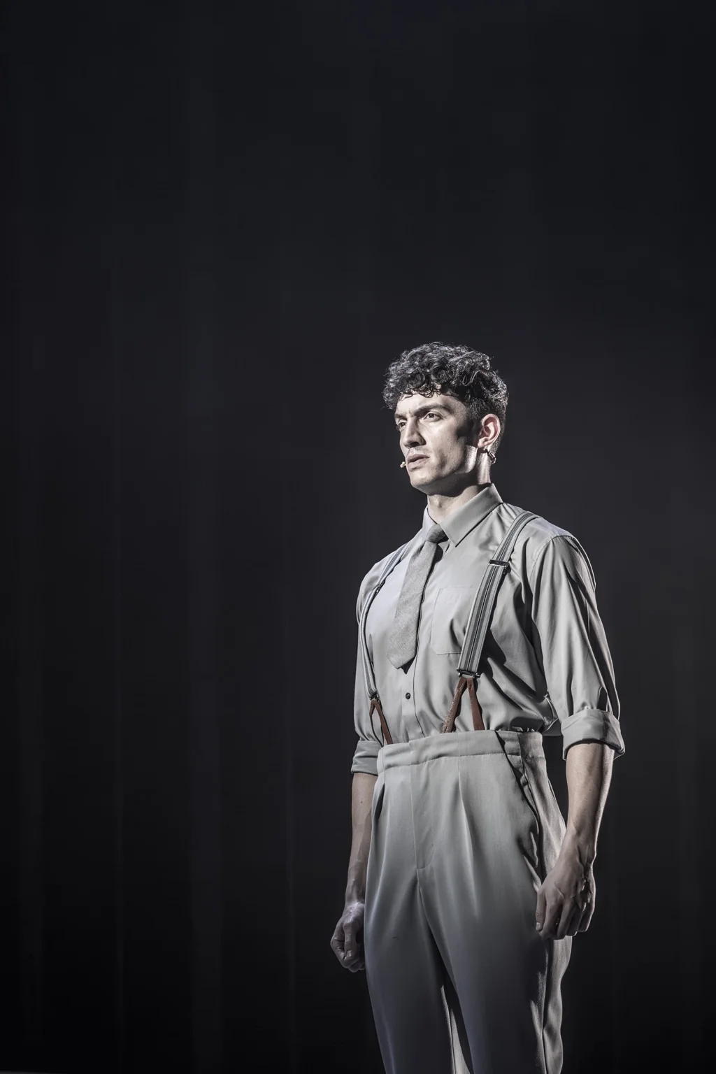 James Olivas as Juan Perón stands alone under a spotlight in Evita.