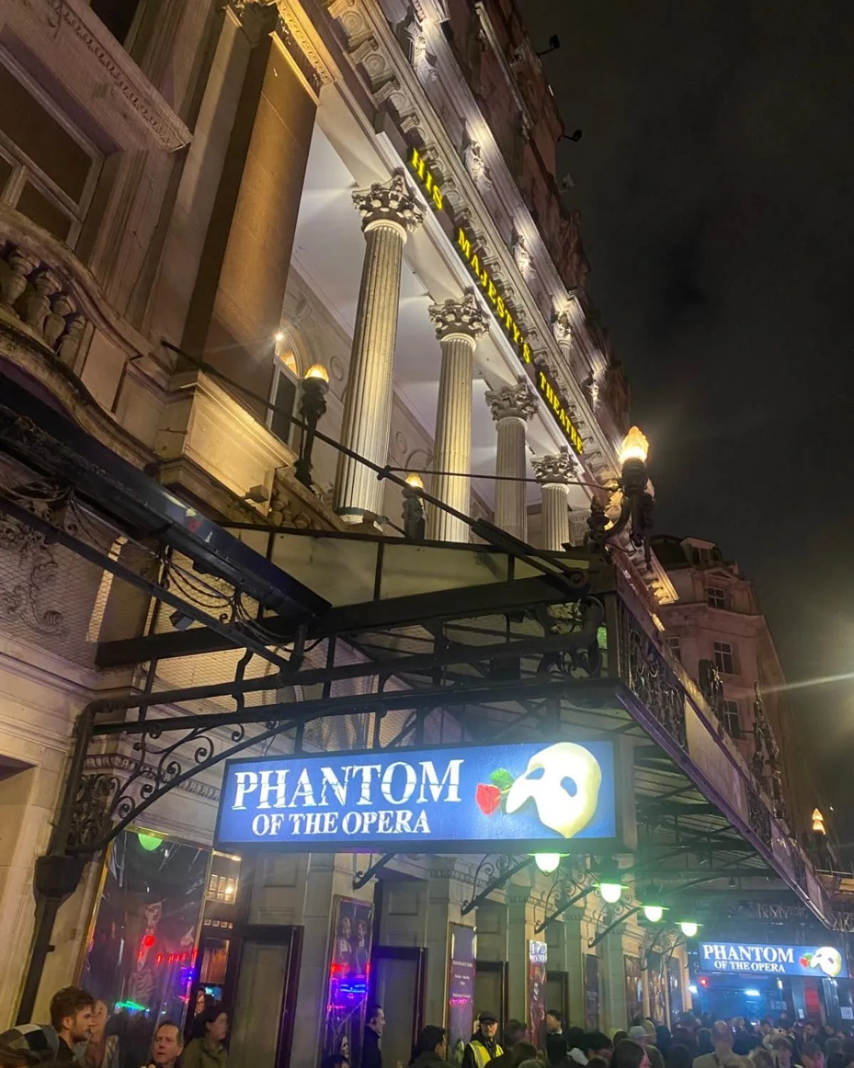 Illuminated entrance of His Majesty's Theatre in London at night with The Phantom of the Opera signage