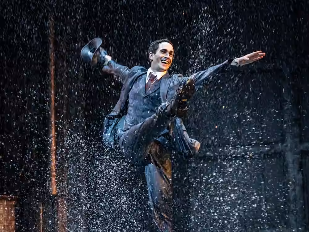 A performer dances through falling rain in the stage production of Singin’ in the Rain.