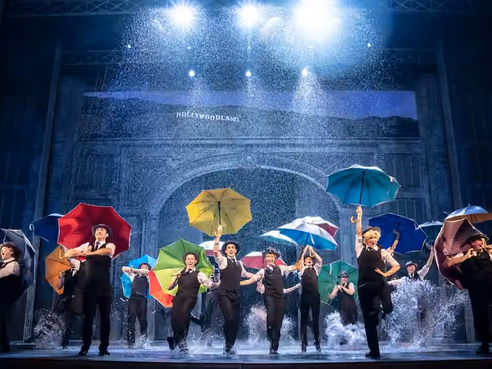 The company dances through falling rain with colourful umbrellas in Singin’ in the Rain.